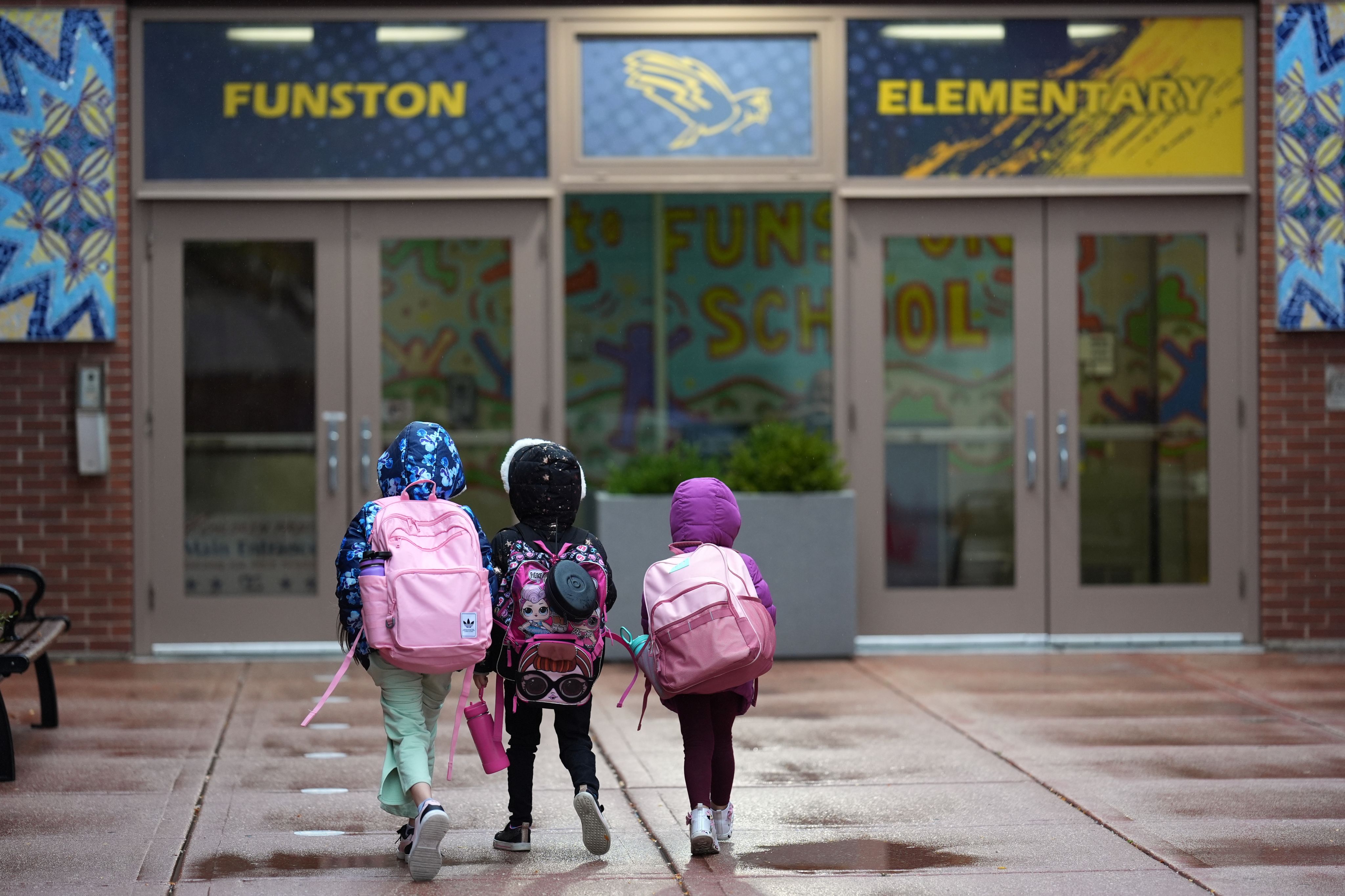 Three sisters, whose single mother fears being mistakenly detained by federal immigration agents because she is of Puerto Rican descent and speaks Spanish, walk into Funston Elementary School in Chicago's Logan Square neighborhood, Oct. 15, 2025. (AP Photo/Rebecca Blackwell)